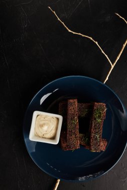 Mavi tabakta kızarmış çavdar ekmeği ve siyah desenli arka plan manzaralı sos.