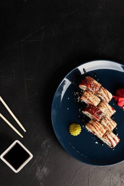 Siyah desenli arka planda mavi bir tabakta yılan balığıyla yuvarlanıyor.