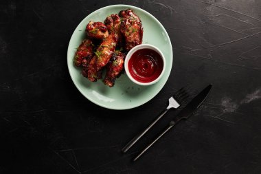 Arka planda siyah desenli bir manzarada açık tabakta ketçaplı tavuk kanatları