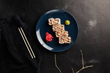 Siyah desenli arka planda mavi bir tabakta yılan balığıyla yuvarlanıyor.