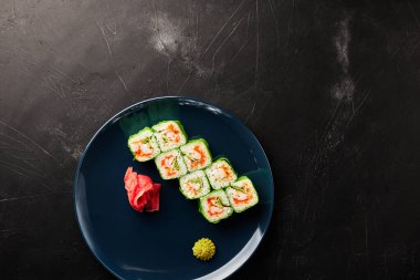 Siyah desenli arka planda mavi bir tabakta yeşil pirinç kağıdına sarılmış.