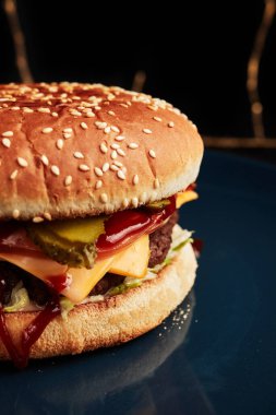 Mavi bir tabakta, siyah bir arka planda, üzerinde altın bir dal olan bir hamburger.