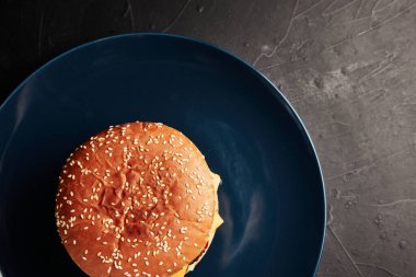 Siyah arka planda mavi bir tabakta altın dallı bir hamburger.