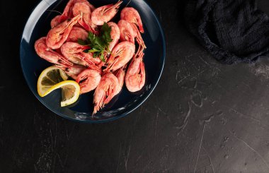 Siyah desenli arka plan görünümlü limonlu mavi tabakta karides.