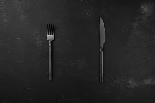 黑色纹理背景上的黑色叉子和刀 — 图库照片