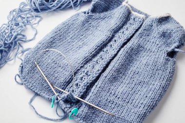 Beyaz arka planda örgü iğneleri üzerine mavi örülmüş ürün