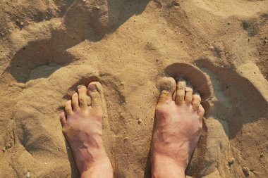 Erkek ayakları kumun üstünde gömülü.