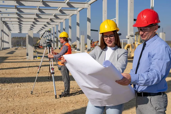 Young Female Architect and Construction Engineer Checking the Blueprint on Construction Site. Gender Equality at Work. Man and Woman in Hardhats Discuss a Construction Project on Site.