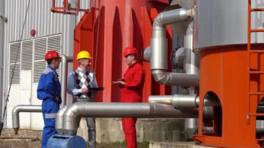 Petrol Rafineri Deposu önünde toplanan iki Petrol İşçisi ve Yöneticisi. İşadamı Üniformalı İki İşçiyle Dijital Tablet Kullanıyor. Dijital Teknoloji ve Takım Çalışması Konsepti.