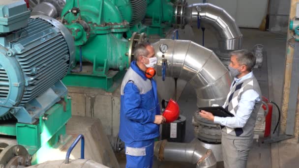 安全衛生責任者Covid 19流行時に工場の従業員の体温を測定するために赤外線額温度計を使用してください 保護顔マスクを着用する管理者及び労働者 — ストック動画