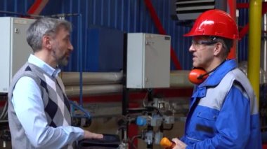 Kişisel Koruyucu Ekipman 'daki Fabrika İşçisiyle İletişim Tableti' ni kullanan İş Adamı Uzaklaştırıldı. Teknik Müdür, Fabrika Salonundaki Bakım İşçisiyle konuşuyor..