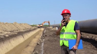 İnşaat Ustabaşı İnşaat Alanındaki Radyo Telekomünikasyon Cihazı 'nı kullanıyor. Görüntüyü büyüt. Kırmızı Hardhat ve Sarı Yelek Giyen İşçi Portresi.