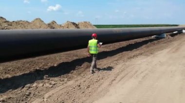 Doğal Gaz Boru Hattı İnşaat Alanında Yürüyen Kırmızı Hardhat İnşaat Müfettişi Drone Bakış Alanı. İnşaat alanında Doğal Gaz Boru Hattı Kurulumunun İlerlemesini Denetleyen Mühendis.