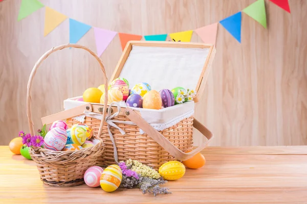 Happy Easter day colorful eggs and flowers in the basket on wooden floor have blurred celebrate banner party flags with copy space.
