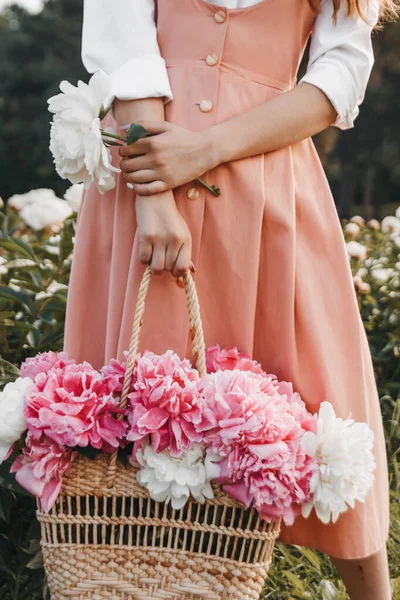 Kadın bahçede dikiliyor ve elinde piyonla bir sepet tutuyor.