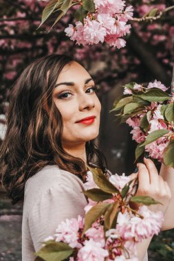 Kadın gülümsüyor ve elinde sakura dalı tutuyor. Bahar portresi.