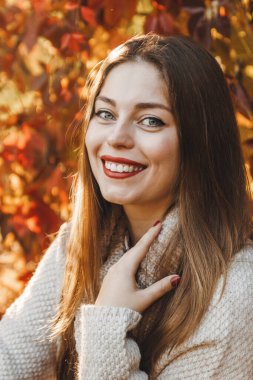 Kız sonbahar zamanı parkta gülüyor ve gülüyor. Kırmızı ruju ve düz uzun saçları var..