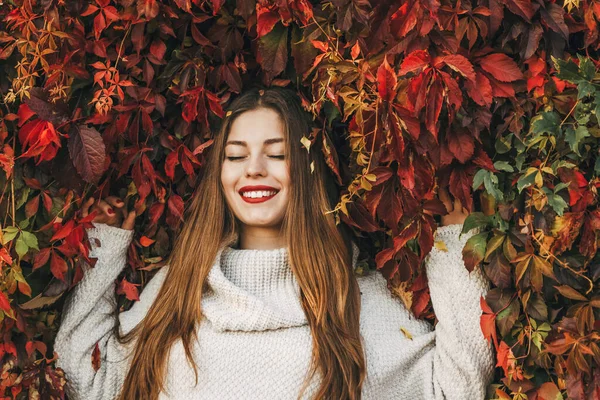 Mutlu kadın kırmızı sarmaşık yapraklarından bir duvarda yatıyor..