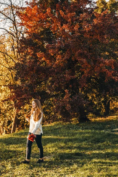 Uzun saçlı genç kadın sonbaharda parkta yürüyor..