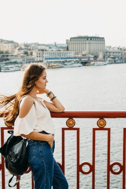 Uzun saçlı kadın nehre bakıyor. Ayakta duruyor.