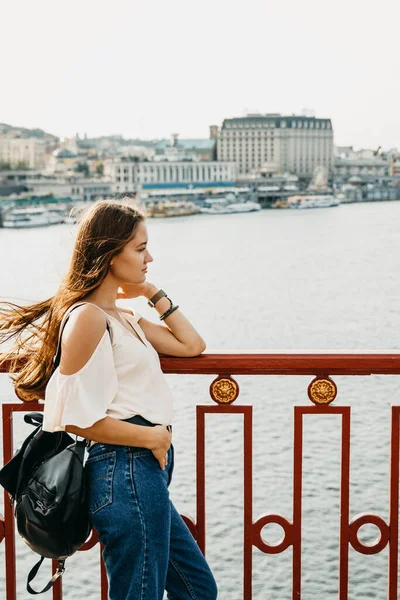 Uzun saçlı kadın nehre bakıyor. Ayakta duruyor.