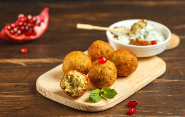 Falafel, ahşap bir tahtanın üzerinde nohut köftesi, sos ve nar tohumları. Koyu ahşap bir masaya yakın çekim