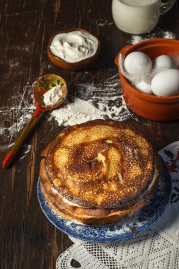 Krep günü. Boyalı tabakta bir yığın krep, eski mutfak gereçleri ve koyu ahşap bir masada pişirme malzemeleri.