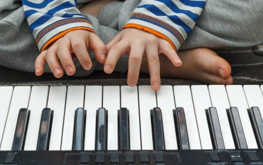 Çocuk yeni bir melodi öğreniyor. Çocuk elleri sentezleyicinin tuşlarında. Evde eğitim. Müzik dersleri. Yakın çekim, seçici odaklanma