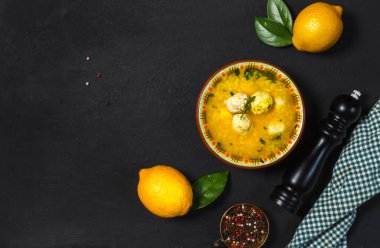 Avgolemono, tavuk suyu, pirinç, yumurta sarısı ve limondan yapılan geleneksel Yunan çorbası. Siyah arka planda düz çizgi. Limonlar, biber değirmeni ve kareli yeşil peçeteyle fotokopi uzayı.