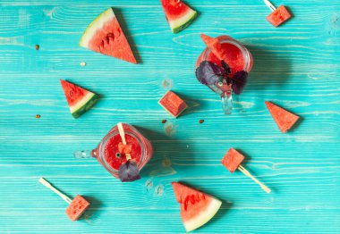 Karpuz ve fesleğen ezmesi kokteyli, ferahlatıcı bir içecek. Mavi ahşap arka planda, karpuz dilimli cam bardaklarda üst manzara.