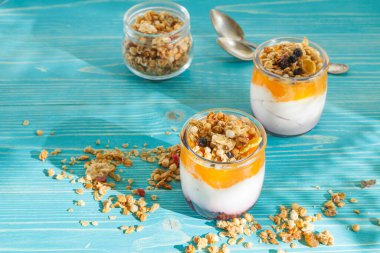 Sağlıklı bir yoğurt, meyve püresi ve granola ile iki fincan. Mavi ahşap bir arka planda, gün ışığında