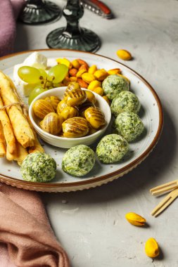 Gri taşlı arka planda bir tabak tapas, arka planda şarap bardağı ve tirbuşon, yakın plan. Kurutulmuş zeytin, safranlı şam fıstığı, ekmek çubuğu ve otlu peynir topları..