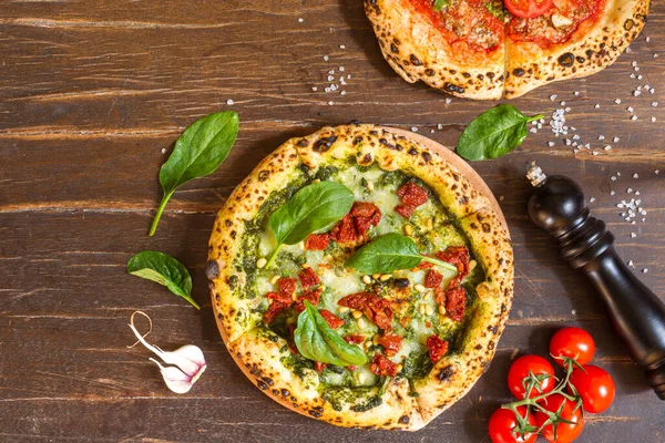 Pizza margarita with spinach, sun-dried tomatoes, pesto sauce, pine nuts, garlic. On a rough wooden background. Top view, copy space, rustic style
