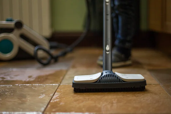 The child washes the tile floor with a steam cleaner, a washing vacuum cleaner. Brush close-up, blurred background