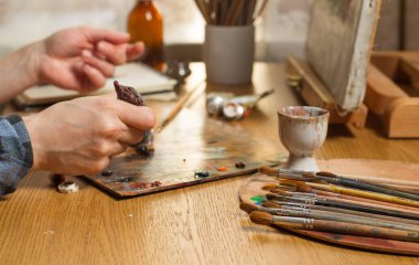 The artists hands squeeze the paint out of the tube onto the palette. Focus on the dirty ones in the foreground