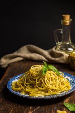Spaghetti with pesto, parmesan and basil leaves in a vintage plate, on a dark wooden table. vertical frame on a black background.