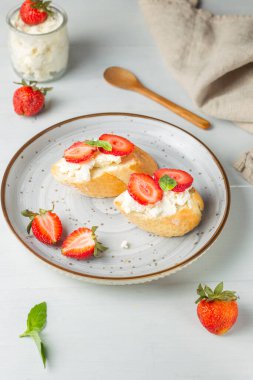 Toast with ricotta, basil and fresh strawberries on a gray plate. Vertical on a light wooden background