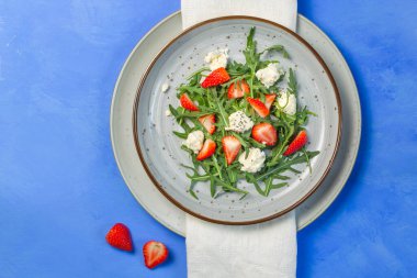 Salad with arugula, strawberries, ricotta and chia seeds. Overhead, on a bright blue background, a copy of the space