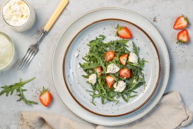 Roka yapraklı lezzetli salata, taze çilek, ricotta ve chia tohumları. Genel olarak, gri arka planda, yatay