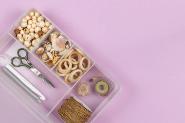 Tahta boncuklar, çocuklar için el işi yüzükler, takılar, çıngıraklar, amigurular. Plastik bir düzenleyicide, yakın plan, üst görünüm, boşluğun kopyası, leylak arka planda yatay