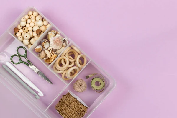 A set of wooden beads, rings for making crafts for children, jewelry, rattles, amigurumi. In a plastic organizer, close-up, top view, copy of the space, horizontal on a lilac background
