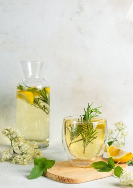 Bir bardak ev yapımı limonata arka planda mürver böğürtlen şurubu ve gaffin, biberiye, nane ve limon dilimleri ile birlikte. Dikey, hafif arkaplanda