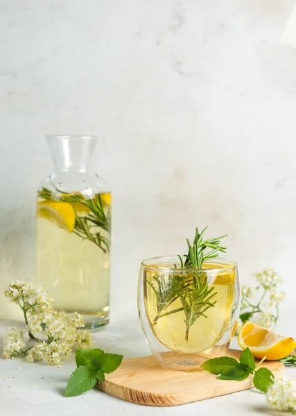 A glass of homemade lemonade made from elderberry syrup and gaffin in the background, with sprigs of rosemary, mint and lemon slices. Vertical, on a light background