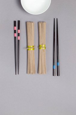 İki porsiyon kuru karabuğday Japon soba eriştesi, iki çift çubuk ve bir kase çorba. Gri arkaplanda düz bir zemin, boşluğun kopyası, dikey