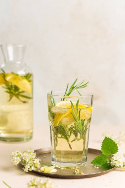 Elderflower şurubu, limon dilimleri, biberiye, nane ve limon yaprağı ile ferahlatıcı içecek. Yuvarlak bakır tepside bir bardak limonata. Dikey, boşluğu kopyala