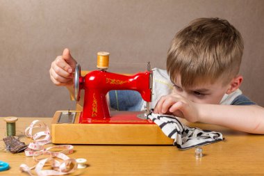 Sarışın çocuk dikiş makinesine iğneyi sokmaya odaklanmış durumda. Portre
