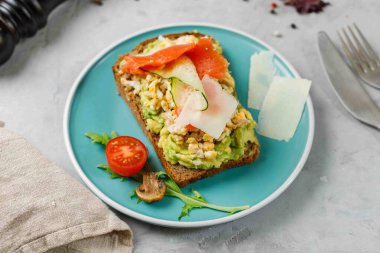Dengeli bir diyet için sağlıklı bir atıştırmalık. Çavdar ekmekli tost, guacamole, çırpılmış somon ve parmesan yaprağı. Beslenme bilimi. Yakın çekim, yatay