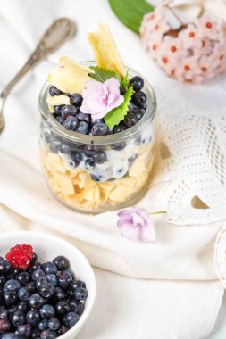 Sağlıklı kahvaltı, yaban mersinli tatlı, waffle ve krema. Dikey, beyaz keten dantelli masa örtüsü üzerinde eski bir kaşık ve taze çiçekler..