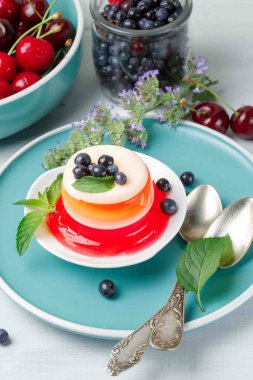 Yaz tatlısı, jöle ya da kirazdan yapılmış panna cotta, yaban mersini. Tabaklara ve kaselere jöle konmuş gri ahşap arka planda, dikey