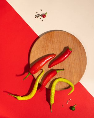 Yuvarlak bir tahta üzerinde sıcak kırmızı ve yeşil biber kabukları. Renkli arkaplanda düz bir zemin, sert gölgeler.